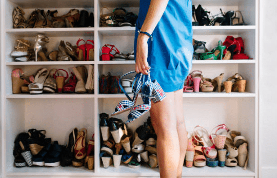 femme portant une robe bleue se tenant devant un placard plein de chaussures